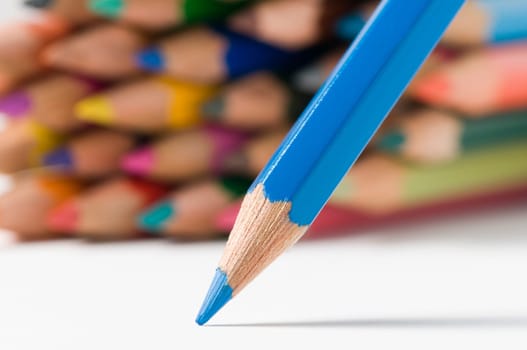 flat-angled detail view of a slanted blue wood colored pencil in front of stacked crayons in the background on drawing paper