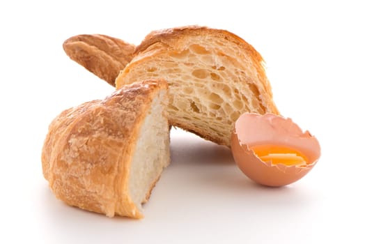 Fresh croissant and raw egg on white background