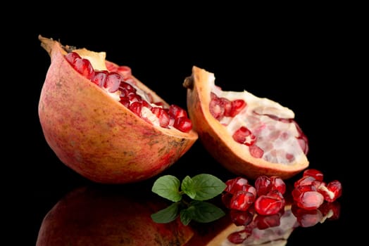 Ripe pomegranate fruit with leaves on black background