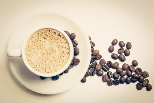 Delicious breakfast cup of coffee top view with foam and roasted bean decoration, vintage filter. Clipping path included, so you can easily copy and paste it on your own design.