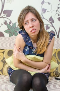 girl holding a pillow over her stomach with a painful expression on her face