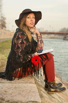 Beautiful brunette girl with a book by the river bank