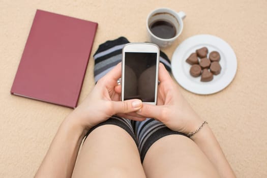 Girl using her phone in bed surrounded by book coffee and dessert