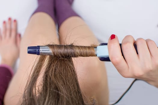 Top view of a girl straightening her hair while sitting in bed