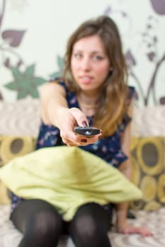 brunette girl with a remote control sitting on a sofa