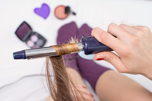 Top view of a girl straightening her hair while sitting in bed