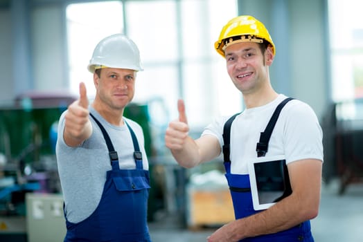 two young worker in factory with thumb up