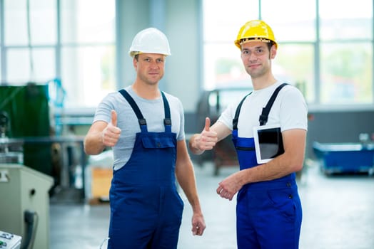 two young worker in factory with thumb up