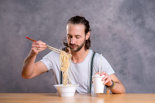 young man eating asian food in front of gray background