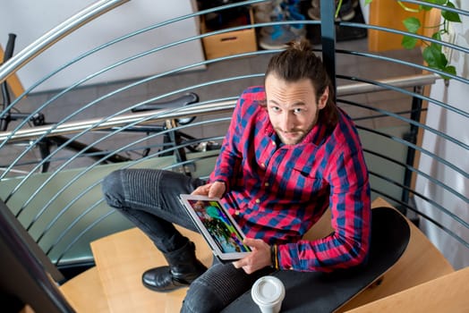 young man in checkered shirt sitting on stairs and using tablet PC