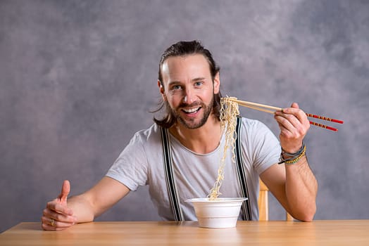 young man eating asian food and smiling in to the camera
