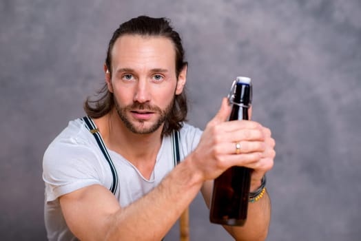 young man in front of gray background opening a beer bottle