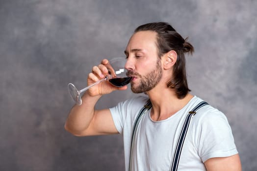 young man in front of gray background drinking red wine