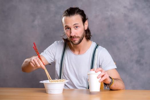 young man eating asian food in front of gray background