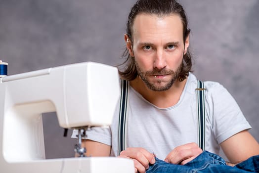 young tailor with sewing machine in front of gray background
