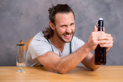 young man in front of gray background opening a beer bottle