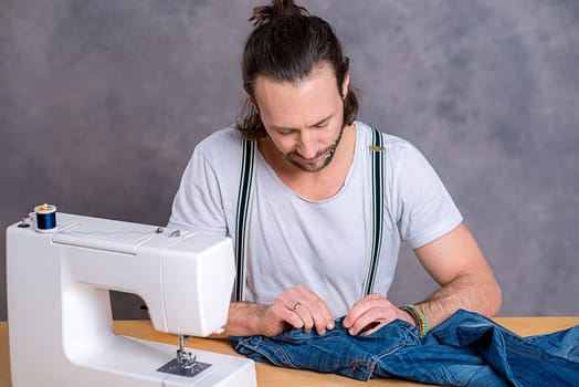 young tailor with sewing machine in front of gray background