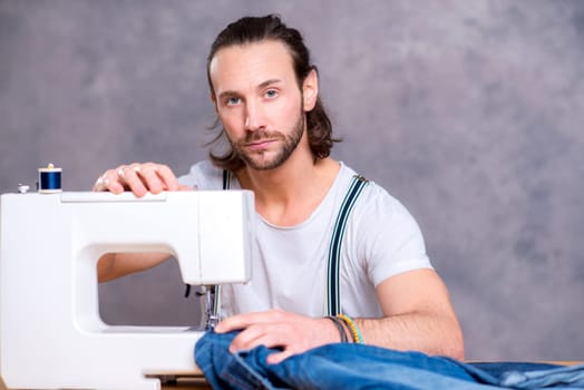 young tailor with sewing machine in front of gray background