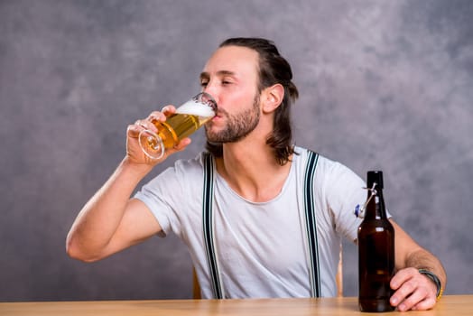 young man in front of gray background drinking beer