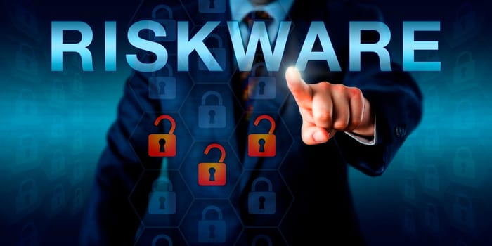 IT specialist is touching RISKWARE on an interactive screen. Three opened virtual padlocks among otherwise intact lock icons embedded in a hexagonal coding matrix signify a possible software risk.