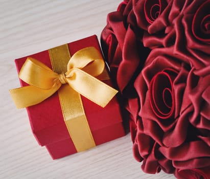 red roses and red gift box with yellow ribbon on wooden surface