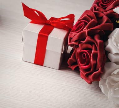 red and white roses and red gift box with yellow ribbon on wooden surface