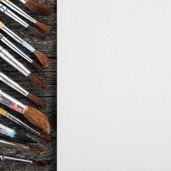 brushes for painting  and blank white paper sheet on vintage wooden  background