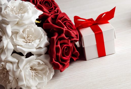 red and white roses and red gift box with yellow ribbon on wooden surface