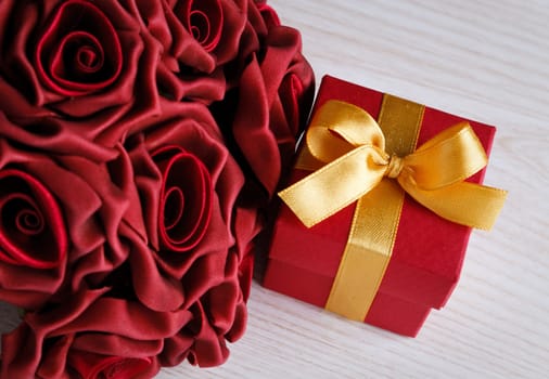 red roses and red gift box with yellow ribbon on wooden surface