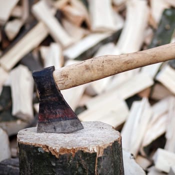 Axe stuck in a stump on a background of chopped firewood