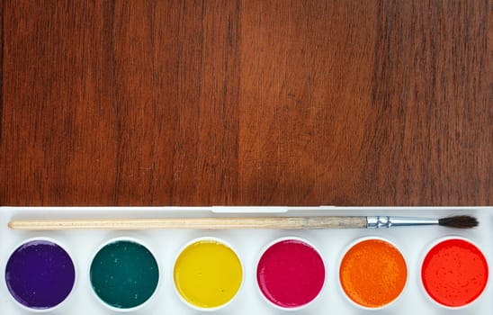 Colorful Aquarelle paints in a box and brushes on wooden background, place for text