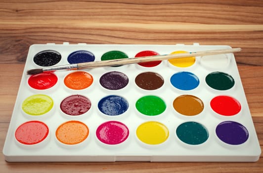 Colorful Aquarelle paints in a box and brushes on  wooden background