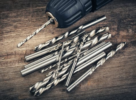 Drill and set of drill bits with screws on wooden background