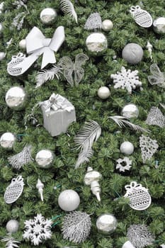 Various silver and glitter ornaments on an artificial green Christmas tree closeup. Green Christmas tree with silver and glitter ornaments background.