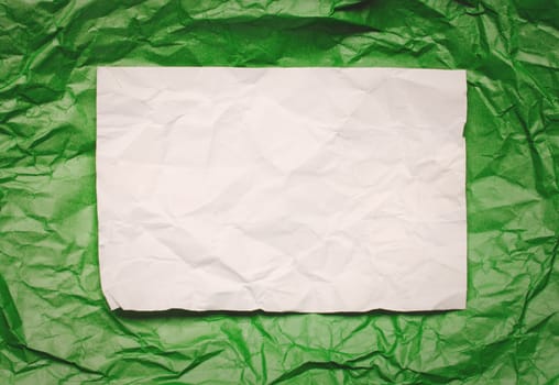 Crumpled  white paper card on green background, place for tex