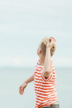 View from behind of a young teenage boy tossing stones into the sea on his summer vacation