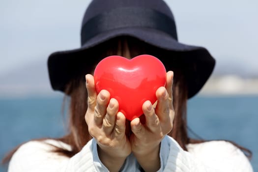 young woman holding red heart in front of her face