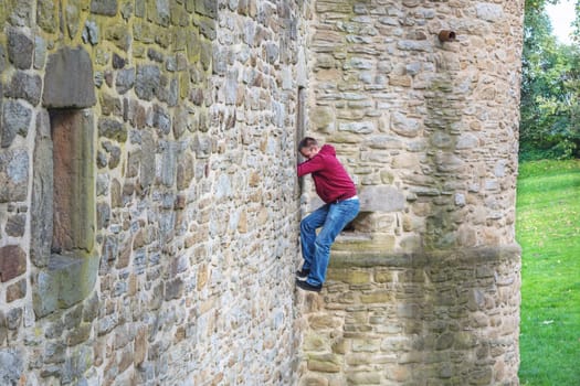 Young adult man climbs up a castle wall.
