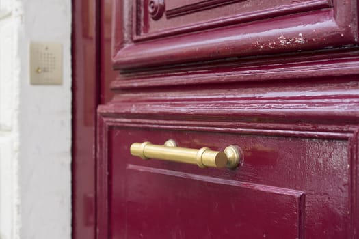 Old brass door handle on sturdy old textured maroon red wooden door