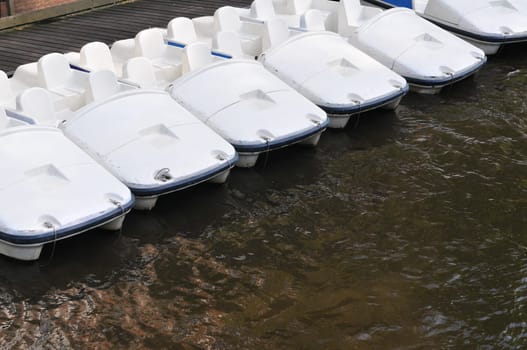 Six white paddle boats for rent in Amsterdam canal.
