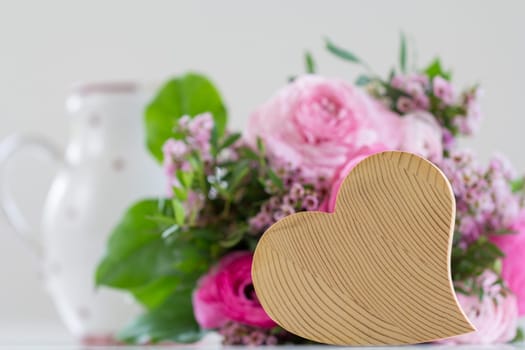 Behind a wooden heart is a bouquet of roses in rose tones on the table - that must be love!