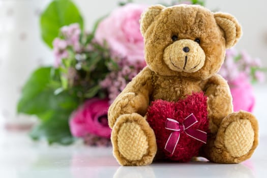 Love you - Teddy bear with heart and in the background a bouquet of flowers
