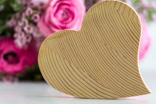 Behind a wooden heart is a bouquet of roses in rose tones on the table - that must be love!