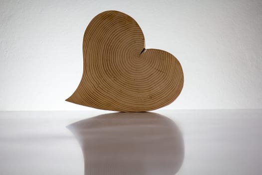 A wooden heart stands on a white surface and is illuminated from behind