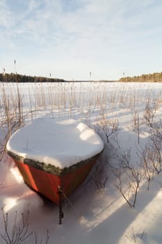Rowboat covered in Snow by lake.