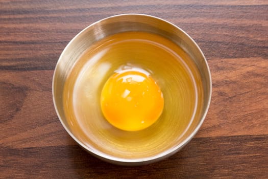 One egg: egg yolks and egg whites in a bowl on a brown worktop