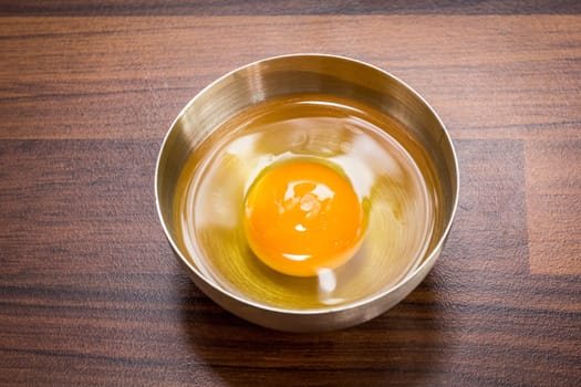 One egg: egg yolks and egg whites in a bowl on a brown worktop