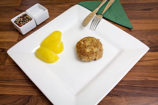 A freshly fried frikadell on a white plate,with potatoes and cutlery