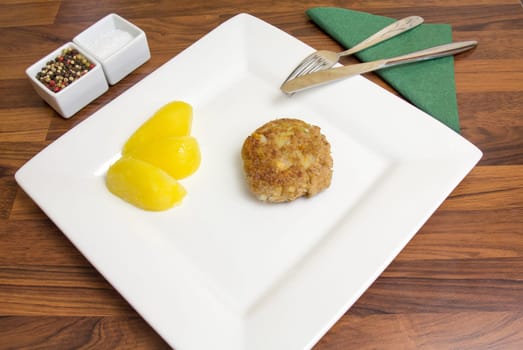 A freshly fried frikadell on a white plate,with potatoes and cutlery
