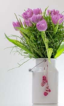 Baby socks hang on a white milk jug in which a bouquet of tulips is stuck